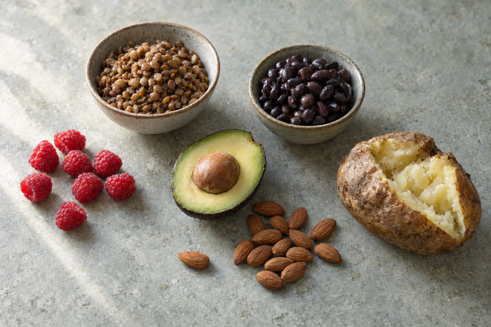 Cooked lentils, black beans, raspberries, half an avocado, almonds and a baked potato with the skin on, laid out on a stone surface